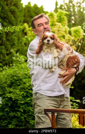 Porträt eines Seniorenmannes mit seinem Hund im Garten. Stockfoto