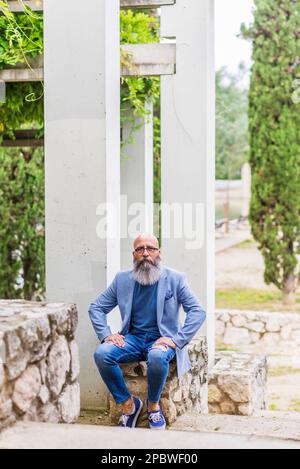 Männlich, mittleren Alters, kahl, bärtiger Mann, der in einem Park sitzt und sich entspannt Stockfoto