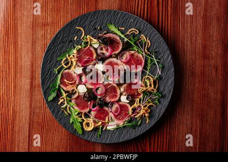 Marmorfleisch-Carpaccio mit Soße und Kräutern auf einem schwarzen Teller Stockfoto