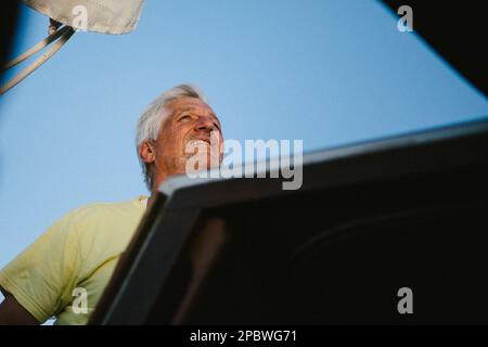 Der Mann segelt sein Boot mit Wind in seinen grauen Haaren mit blauem Himmel Stockfoto