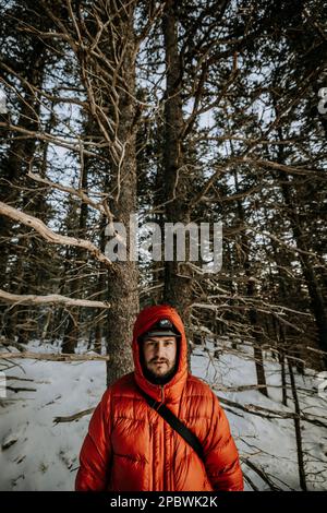 Porträt eines jungen Mannes im Winter mit orangefarbener Puffjacke mit Kapuze. Stockfoto