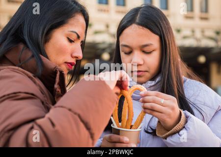 Mutter und Tochter essen Churros mit Schokolade auf der Straße. Stockfoto