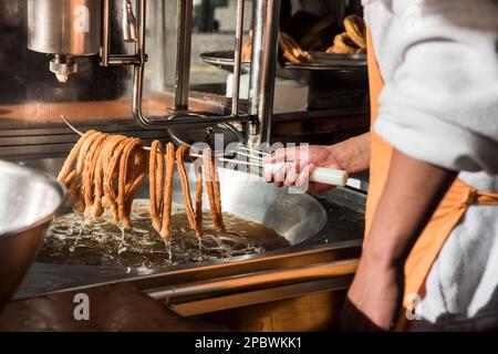 Detailfoto eines Arbeiters, der die Churros aus dem heißen Öl entfernt Stockfoto