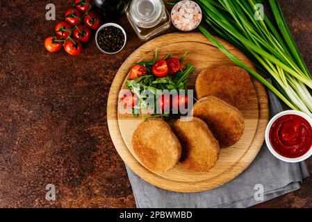 Hühnerschnitzel auf einem Holzbrett. Gemüse und Kräuter Stockfoto