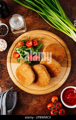 Hühnerschnitzel auf einem Holzbrett. Gemüse und Kräuter Stockfoto