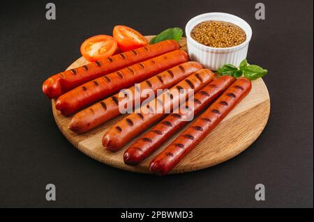 Gegrillte Würstchen auf einem Holzbrett. Gemüse und Sauce. Stockfoto