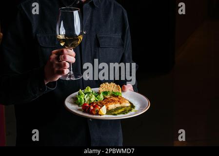 Ein Mann hält einen Teller mit gegrilltem Fisch Stockfoto