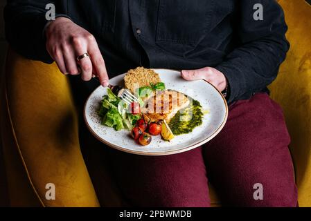 Ein Mann isst gegrillten Fisch mit Beilagen und Gemüse Stockfoto