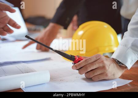 Ein Team von Ingenieuren oder Technikern hält ein Walkie-Talkie und plant mit Bauplan und Bauwerkzeugen auf dem Konferenztisch an der con Stockfoto