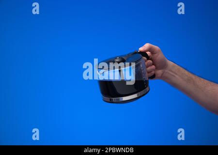 Hausgemachte große Kaffeekanne aus Glas, die ein Mann mit einer Gießgeste in der Hand hält. Nahaufnahme des Studios, isoliert auf blauem Hintergrund. Stockfoto