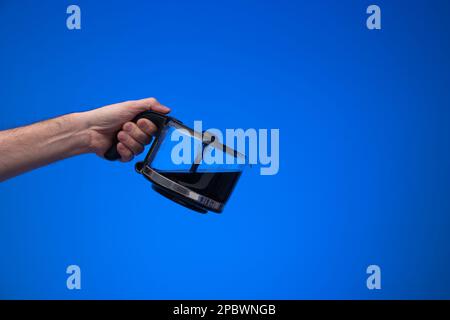 Hausgemachte große Kaffeekanne aus Glas, die ein Mann mit einer Gießgeste in der Hand hält. Nahaufnahme des Studios, isoliert auf blauem Hintergrund. Stockfoto