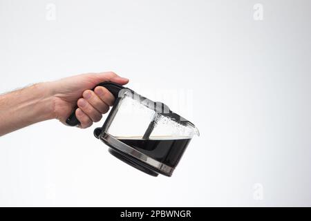 Hausgemachte große Kaffeekanne aus Glas, die ein Mann mit einer Gießgeste in der Hand hält. Nahaufnahme des Studios, isoliert auf weißem Hintergrund. Stockfoto