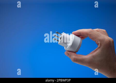 Steckdosenadapter in Schweizer Ausführung, der mit dem Stecker in der Hand gehalten wird. Nahaufnahme im Studiostil, isoliert auf blauem Hintergrund. Stockfoto