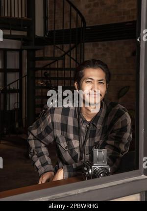 Porträt eines jungen Mannes, der am Fenster eines Coffeeshop in Bangkok sitzt Stockfoto