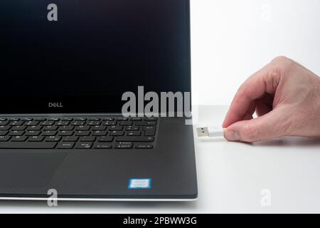 USB-Speicherstick oder Ladekabel, das von einem kaukasischen Stecker in den Laptop-Anschluss gesteckt wird. Nahaufnahme des Studios, isoliert auf weißem Hintergrund. Stockfoto