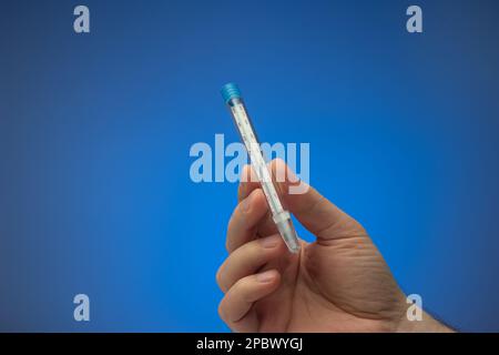 Quecksilberglasthermometer in der Hand eines weißen Mannes. Nahaufnahme des Studios, isoliert auf blauem Hintergrund. Stockfoto