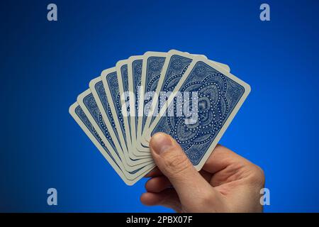 Hand auf Spielkarten, die ein weißer Mann in der Hand hält. Nahaufnahme des Studios, isoliert auf blauem Hintergrund. Stockfoto