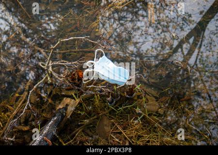 Covid-Gesichtsmasken-Wurf. Weggeworfene Gesichtsmaske in einer Waldpfütze. Tagsüber, keine Leute. Stockfoto