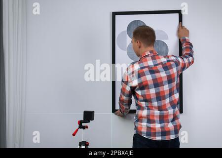 Mann, der eine Kreuzlinienlaser-Wasserwaage zum Aufhängen von Malerarbeiten an eine helle Wand verwendet, Rückansicht Stockfoto