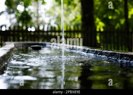 Sauberer Wasserstrahl, der im Freien in einen geschnitzten Baumstamm fließt. Nahaufnahme, geringe Schärfentiefe, keine Menschen Stockfoto