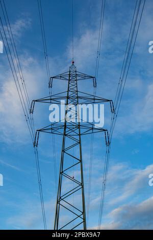 Große Stromleitungen mit Metallträgern in Europa. Niedriger Winkel, wolkiger blauer Himmelshintergrund, keine Menschen. Stockfoto