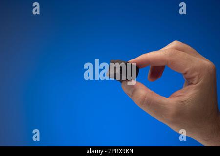 Praline, Trüffel oder Süßigkeiten aus dunkler Schokolade, die ein weißer Mann in der Hand hält. Nahaufnahme des Studios, isoliert auf blauem Hintergrund. Stockfoto