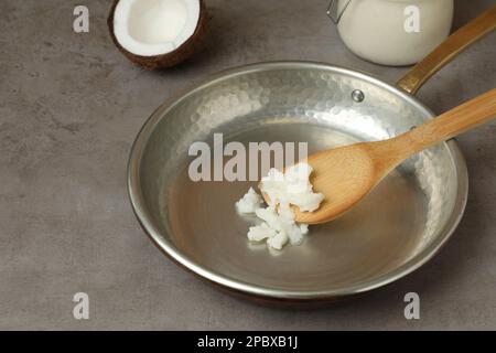 Bratpfanne mit Kokosöl und Holzspachtel auf grauem Tisch. Gesundes Kochen Stockfoto