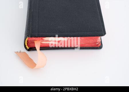 Altes, schwarzes, geschlossenes, festes Buch mit Satin-Lesezeichen. Nahaufnahme, geringe Tiefenschärfe, weißer Hintergrund, keine Menschen Stockfoto