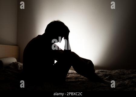 Männliche Silhouette, die Einsamkeit oder Depression in seinem Apartmentbett darstellt. Stockfoto