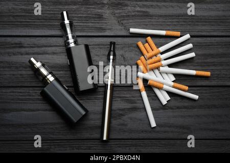 Zigaretten und verschiedene Dämpfe auf schwarzem Holzhintergrund, flach liegend. Raucheralternative Stockfoto