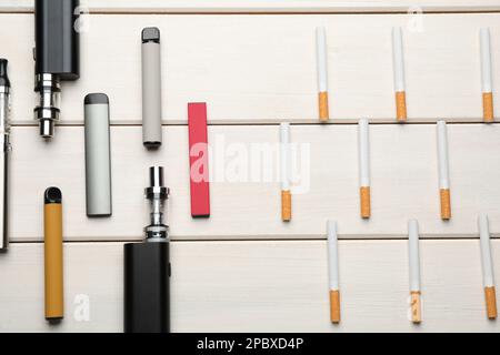 Verschiedene Dampfgeräte und Zigaretten auf weißem Holztisch, flach liegend. Raucheralternative Stockfoto