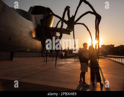 Bilbao, Spanien - 02. August 2022: Ein paar Touristen machen ein Selfie bei Sonnenuntergang neben der Spinne, der Skulptur von Louise Bourgeois mit dem Titel Mamam in Th Stockfoto