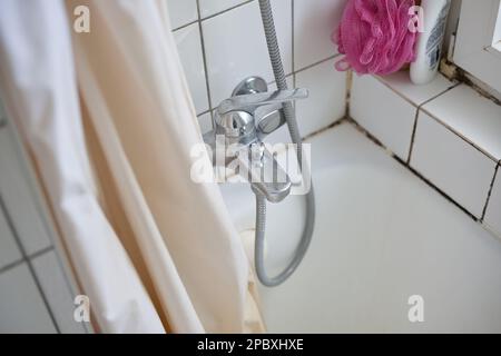 Alte dreckige Badewanne, Duschvorhang und Wasserhahn in einem Apartment-Badezimmer. Blick von oben, weiße Faienzwand, keine Menschen. Stockfoto