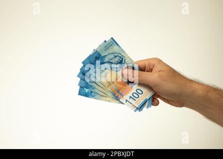 100 Schweizer-Franken-Banknoten, die ein weißer Mann in der Hand hält. Nahaufnahme des Studios, isoliert auf weißem Hintergrund. Stockfoto