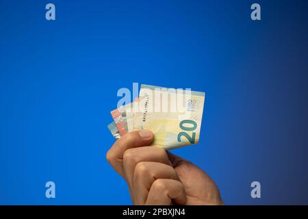 Ein Spread von 20-, 10- und 5-Euro-Banknoten, die ein weißer Mann in der Hand hält. Nahaufnahme des Studios, isoliert auf blauem Hintergrund. Stockfoto