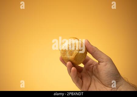 Hausgemachtes, kleines Panini-Brötchen mit Backofensockel, das von männlichen Kaukasiern in der Hand gehalten wird. Nahaufnahme des Studios, isoliert auf orangefarbenem Hintergrund. Stockfoto