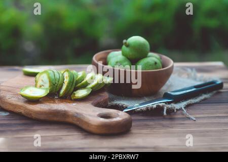 Gesunde Ernährung. Walnüsse, in Scheiben geschnitten, werden auf einem Schneidebrett verstreut. Alter Vintage-Tisch und ganze unreife Walnussfrüchte. Stockfoto