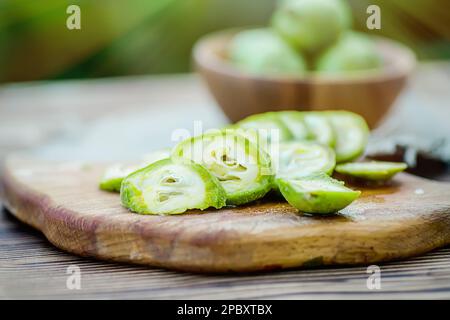 Gesunde Ernährung. Walnüsse, in Scheiben geschnitten, werden auf einem Schneidebrett verstreut. Alter Vintage-Tisch und ganze unreife Walnussfrüchte. Stockfoto