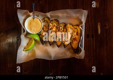 Gebackene Muscheln mit Käsesauce, serviert mit Limettenscheiben Stockfoto