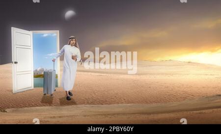Ein arabischer Mann mit Keffiyeh, der ein Handy mit einem Koffer in der Hand hält und durch die Wüste läuft Stockfoto