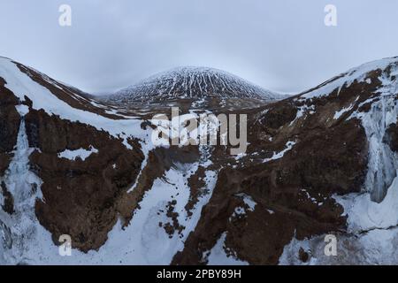 Weitwinkelblick auf schneebedeckte Berge unter wolkenlosem, düsterem Himmel in Island Stockfoto