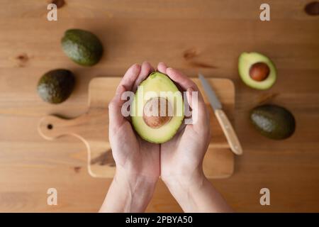 Draufsicht einer anonymen Person, die Avocado über einem Holztisch hält Stockfoto