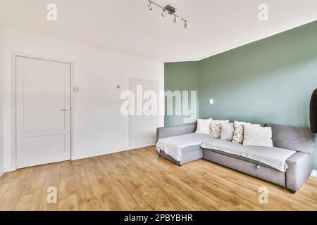 Komfortables Sofa mit Kissen an der Wand im modernen Apartment mit minimalistischer Innenausstattung und Parkettboden Stockfoto