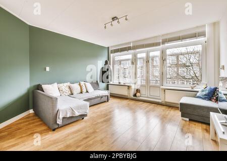 Komfortables Sofa mit Kissen an der Wand im modernen Apartment mit minimalistischer Innenausstattung und Parkettboden Stockfoto