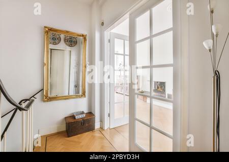 Innenseite des Flurs mit Treppe und Spiegel in der Nähe weißer Glastüren in einem geräumigen Luxushaus Stockfoto