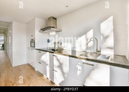 Inneneinrichtung einer stilvollen offenen Küche mit weißen Schränken und eingebauten Geräten in einem offenen Raum Stockfoto