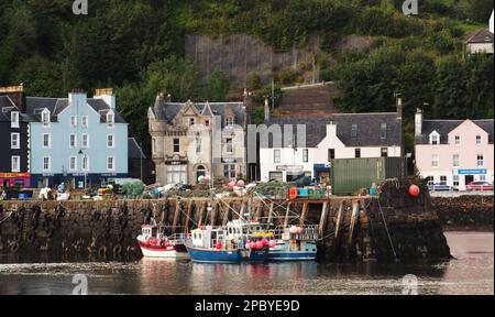 Die farbenfrohen Strandhotels und der Pier in Tobermory, Mull, Schottland mit Fischerbooten im Vordergrund Stockfoto