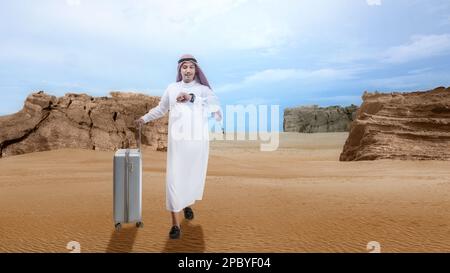 Ein arabischer Mann mit Keffiyeh, der auf die Uhr am Handgelenk schaut, mit einem Koffer, der durch die Wüste geht Stockfoto