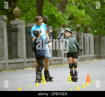 Rollerblading. Mann Trainer herumtöricht mit Jungen in einem Park. 25. Juni 2019. Kiew, Ukraine Stockfoto