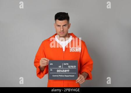 Verbrecherfoto eines Gefangenen im orangefarbenen Overall mit Brett auf grauem Hintergrund, Vorderansicht Stockfoto